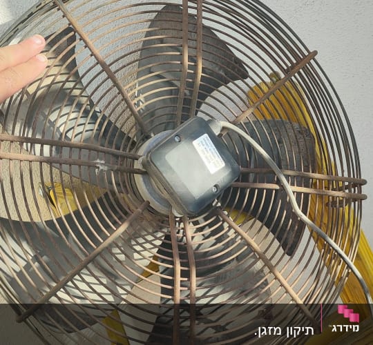 מאוורר תעשייתי על סולם צהוב ליד קיר